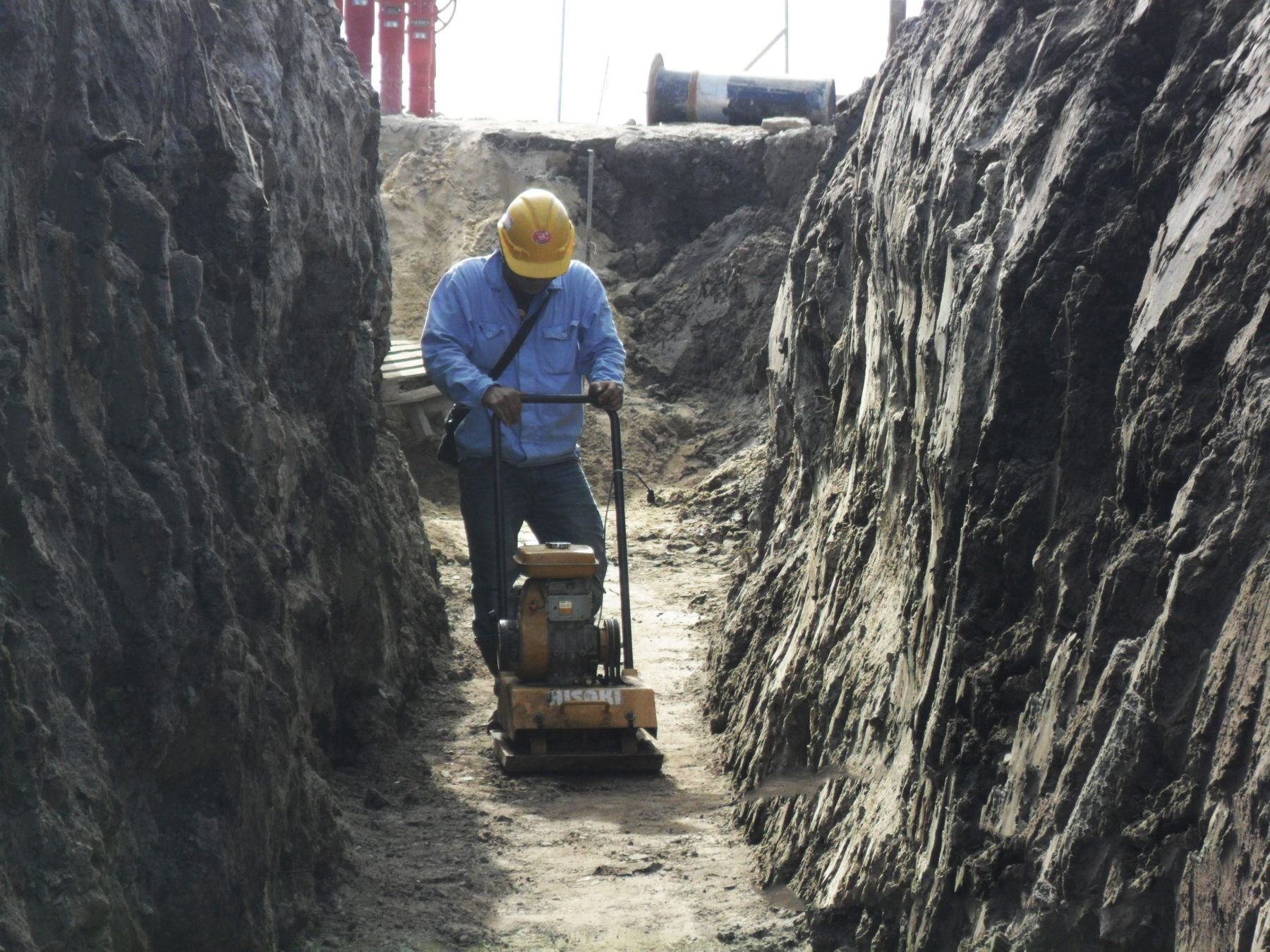 Worker compacting soil in a trench with safety gear